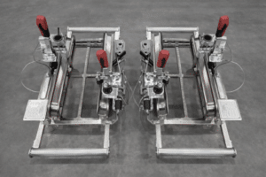 Deux dispositifs de serrage industriels en inox avec poignées rouges et schémas techniques sur sol gris.