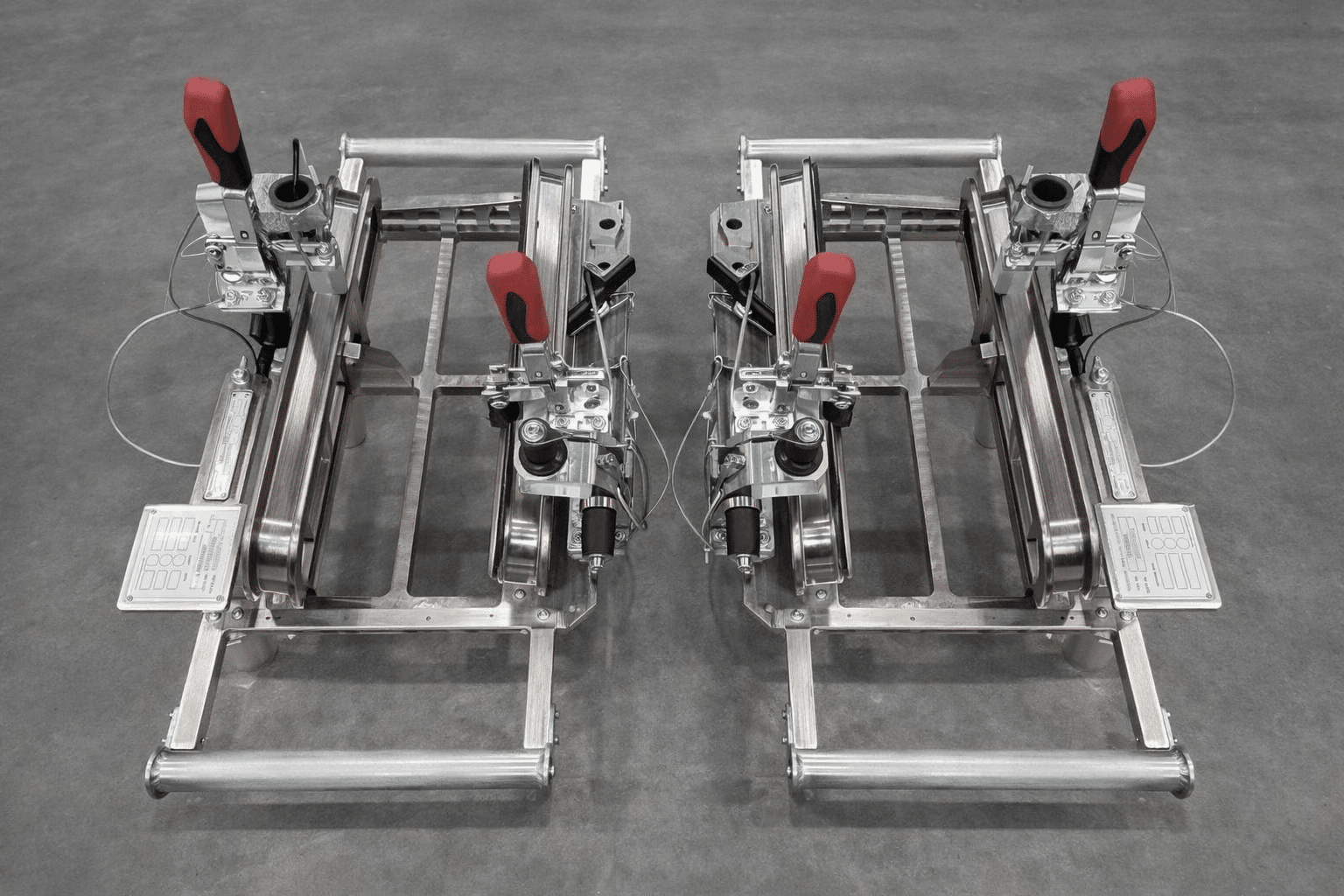 Deux dispositifs de serrage industriels en inox avec poignées rouges et schémas techniques sur sol gris.