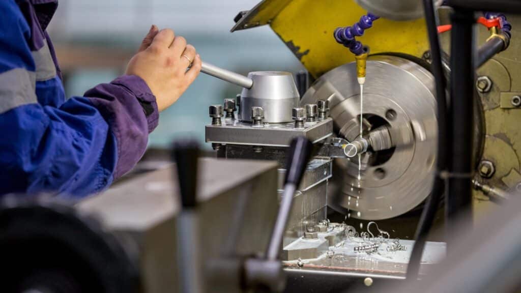 Main d'un tourneur actionnant un tour industriel sur une pièce métallique avec liquide de coupe et copeaux.